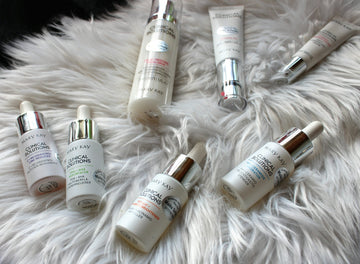 Six skincare bottles and tubes arranged on a soft white faux fur surface