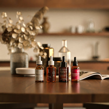 Four amber glass dropper bottles of facial oil on a wooden table
